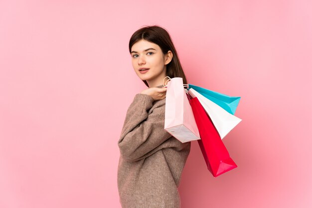 Young Ukrainian teenager woman over isolated pink wall holding shopping bags and smiling