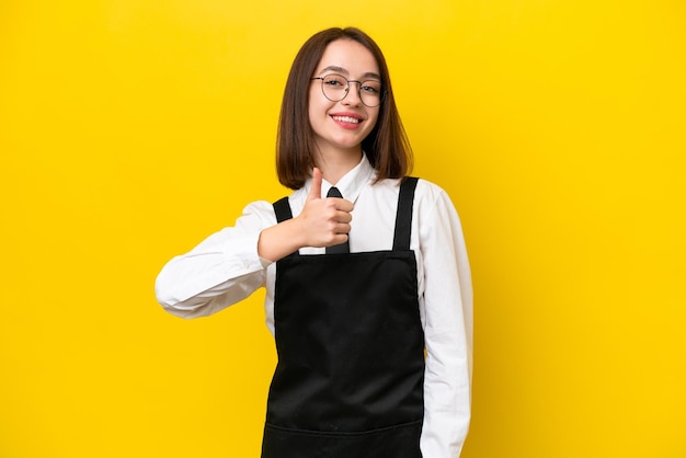 Young ukrainian waitress woman isolated on yellow background giving a thumbs up gesture