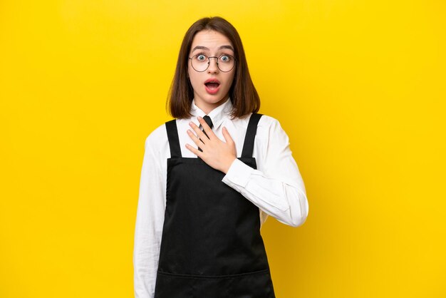 Young ukrainian waitress woman isolated on yellow background surprised and shocked while looking right