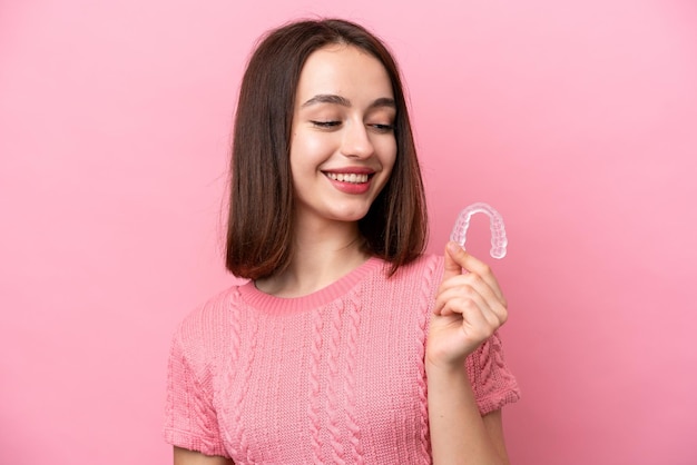 Young Ukrainian woman holding invisible braces isolated on pink background with happy expression