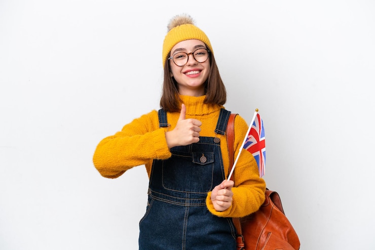 Photo 親指を立てるジェスチャーを与える白い背景で隔離のイギリスの旗を保持している若いウクライナの女性