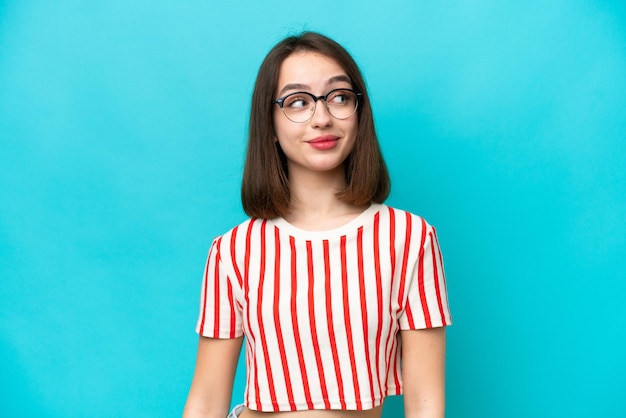 Young Ukrainian woman isolated on blue background making doubts gesture looking side