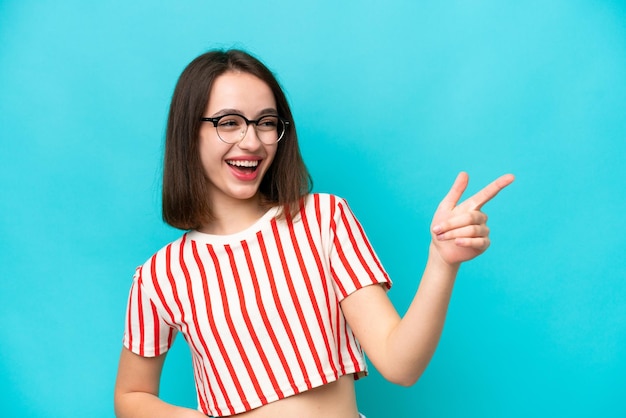 Young Ukrainian woman isolated on blue background pointing finger to the side and presenting a product