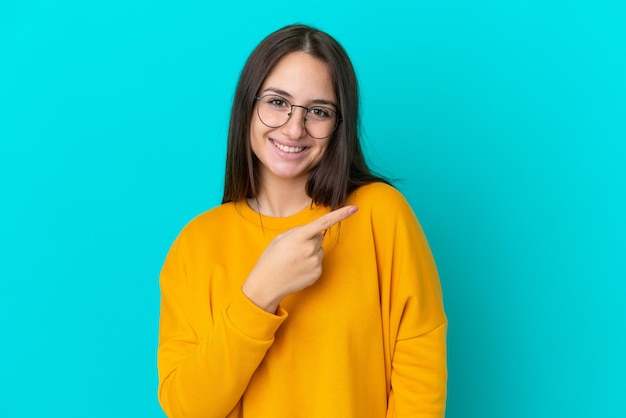 Young Ukrainian woman isolated on blue background With glasses and pointing side