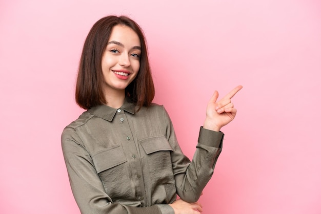 Young Ukrainian woman isolated on pink background pointing finger to the side