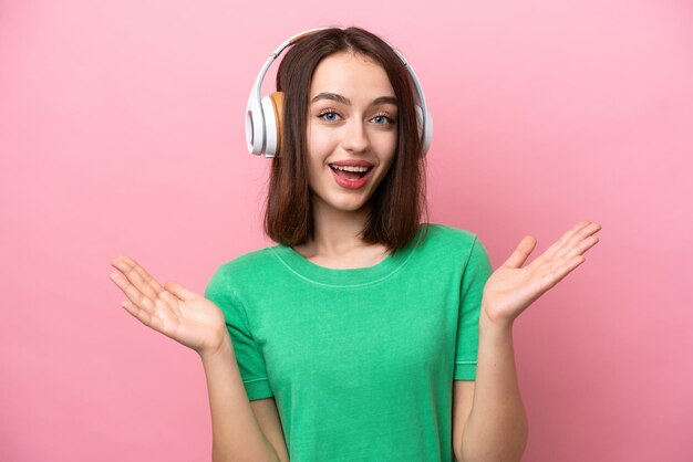 Young Ukrainian woman isolated on pink background surprised and listening music