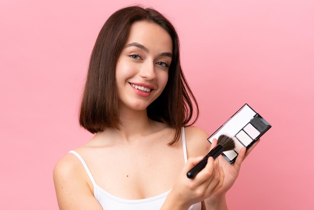 Young Ukrainian woman isolated on pink background with makeup palette and happy