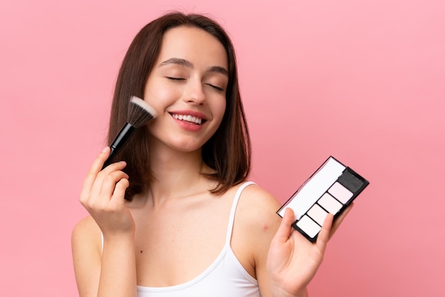 Young Ukrainian woman isolated on pink background with makeup palette and happy