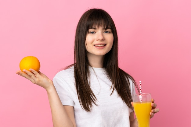 Young Ukrainian woman isolated on pink wall holding an orange and an orange juice