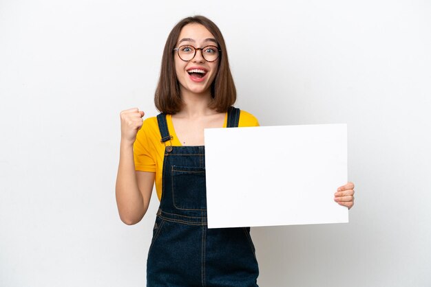 Young Ukrainian woman isolated on white background holding an empty placard and celebrating a victory