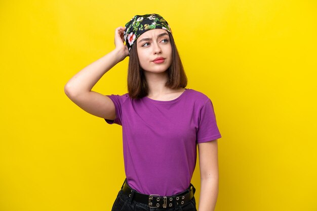 Young Ukrainian woman isolated on yellow background having doubts while scratching head