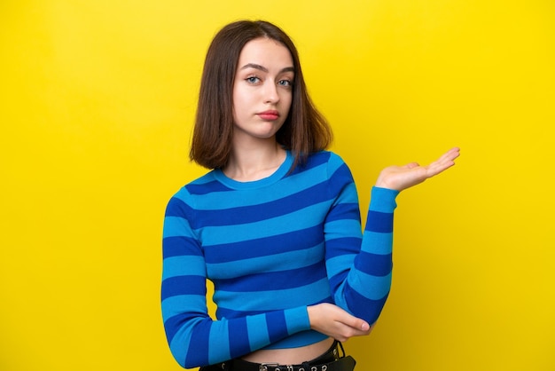 Young Ukrainian woman isolated on yellow background having doubts