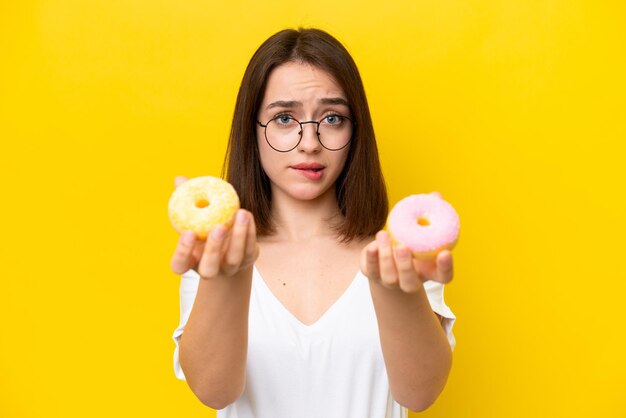 Young ukrainian woman isolated on yellow background holding a donut and sad