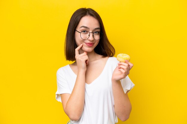 Young Ukrainian woman isolated on yellow background holding a donut