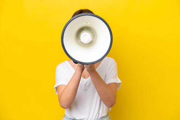 Young Ukrainian woman isolated on yellow background shouting through a megaphone to announce something