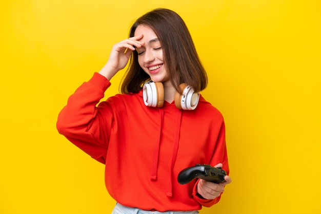 Young ukrainian woman playing with a video game controller isolated on yellow background laughing