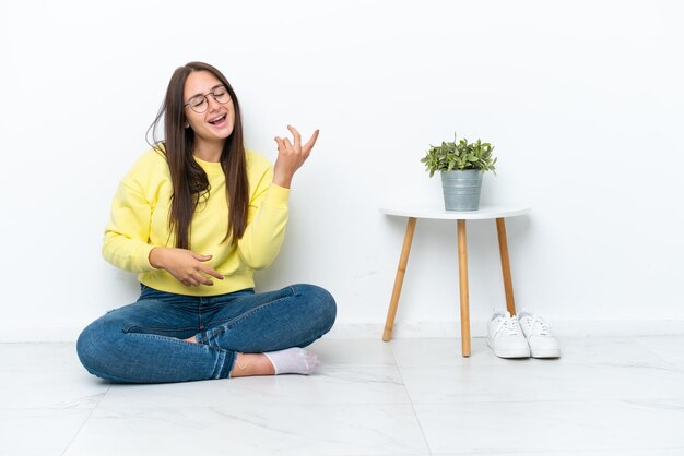 Foto giovane donna ucraina seduta sul pavimento della sua casa isolata sul muro bianco che fa un gesto di chitarra