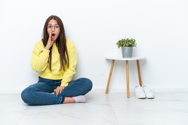 Young Ukrainian woman sitting on the floor of her house isolated on white wall with surprise and shocked facial expression