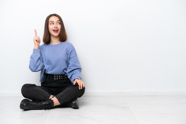 Young Ukrainian woman sitting on the floor isolated on white background intending to realizes the solution while lifting a finger up