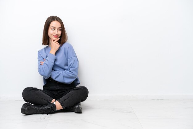 Young Ukrainian woman sitting on the floor isolated on white background looking to the side