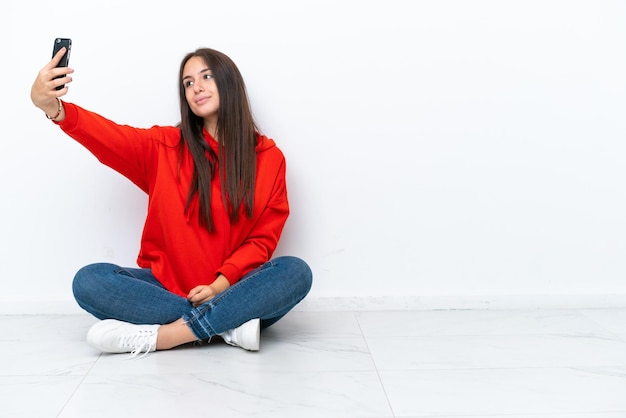 Young Ukrainian woman sitting on the floor isolated on white background making a selfie
