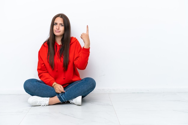 人差し指で指している白い背景で隔離の床に座っている若いウクライナの女性素晴らしいアイデア