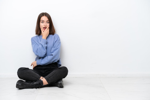 Young Ukrainian woman sitting on the floor isolated on white background surprised and shocked while looking right