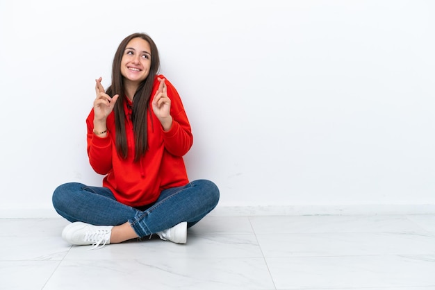 Young Ukrainian woman sitting on the floor isolated on white background with fingers crossing