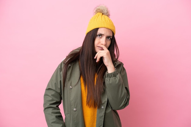 Young ukrainian woman wearing winter jacket isolated on pink\
background having doubts and with confuse face expression