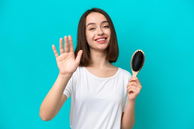 Young ukrainian woman with hair comb isolated on blue background saluting with hand with happy expression