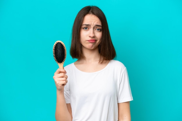 Young ukrainian woman with hair comb isolated on blue background with sad expression