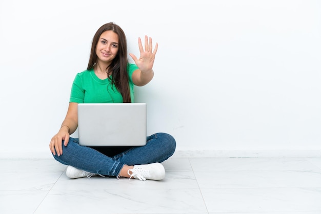 Young Ukrainian woman with a laptop sitting on floor counting five with fingers