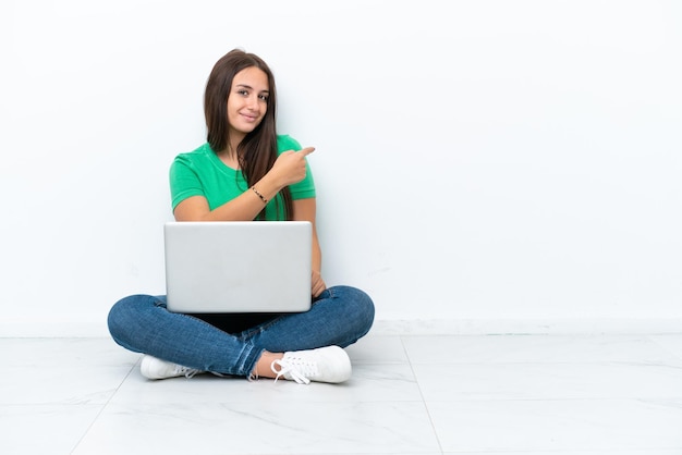 Young Ukrainian woman with a laptop sitting on floor pointing back