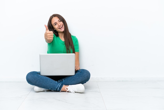 Young Ukrainian woman with a laptop sitting on floor with thumbs up because something good has happened