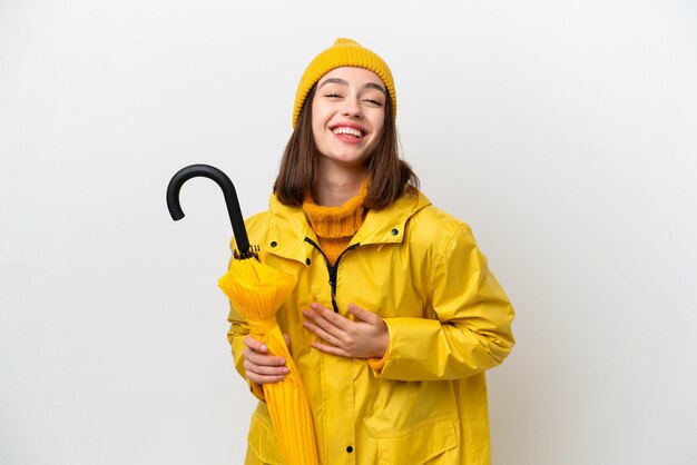 Young Ukrainian woman with rainproof coat and umbrella isolated on white background smiling a lot