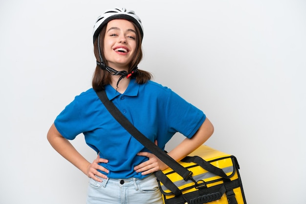 Young Ukrainian woman with thermal backpack isolated on white background posing with arms at hip and smiling