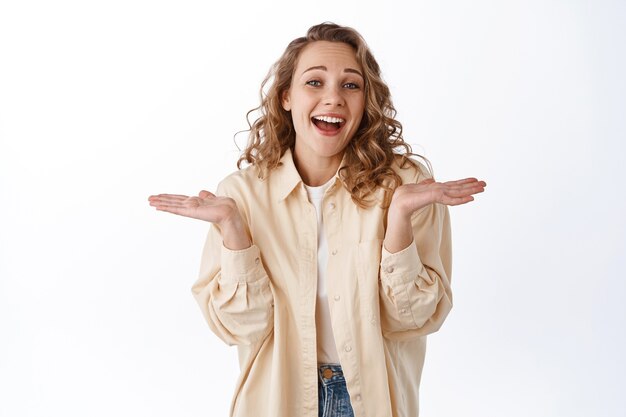 Giovane ragazza indifferente, ridendo e alzando le spalle con un sorriso felice, non lo so e non mi interessa, in piedi sul muro bianco