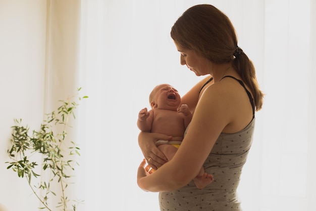 泣いている新生児を両腕に抱えている冷静な若い母親産後うつ病の女性は、泣いている赤ちゃんを落ち着かせる力がありません。家で孤独に疲れ果てた母親