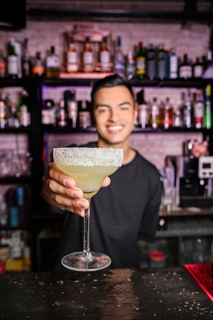 A young unfocused mixologist shows a margarita cocktail on camera