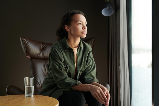 Young unhappy African American woman sitting in front of large window