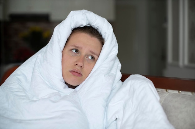 Young unhappy depressed girl woman covering herself in blanket with sad frustrated look at home in