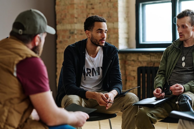 Young unhappy man sharing his problems with other attandants of session