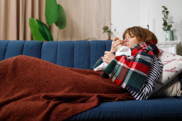 Young unhappy woman lying on the couch with a cold. Girl is sick on seasonal respiratory diseases