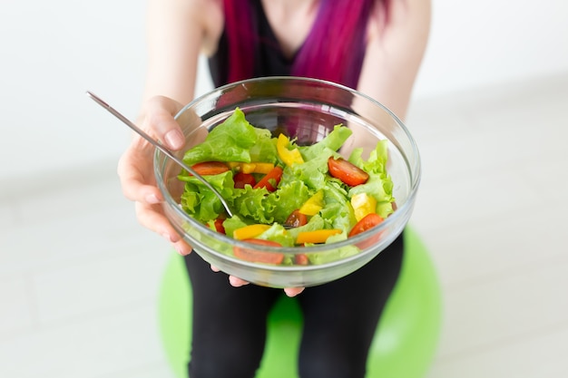 Young unidentified fitness blogger girl holding vegetable salad and measuring tape. Concept of sports lifestyle and proper nutrition