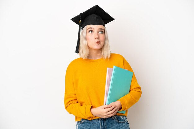 Young university caucasian woman graduate isolated on white background and looking up