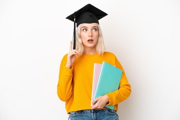 Young university caucasian woman graduate isolated on white background thinking an idea pointing the finger up