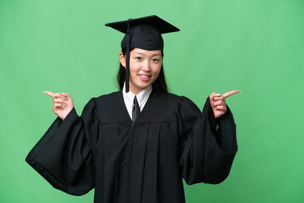 年轻的大学毕业生亚洲女人在孤立的背景指着手指向侧面和快乐