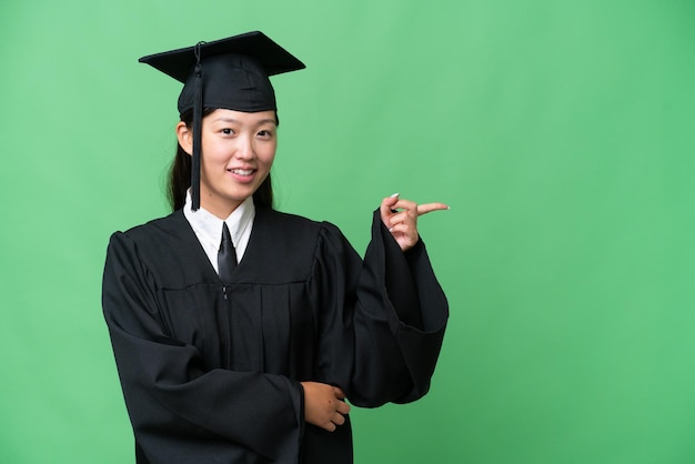 年轻的大学毕业生亚洲女人在孤立的背景上指着一边