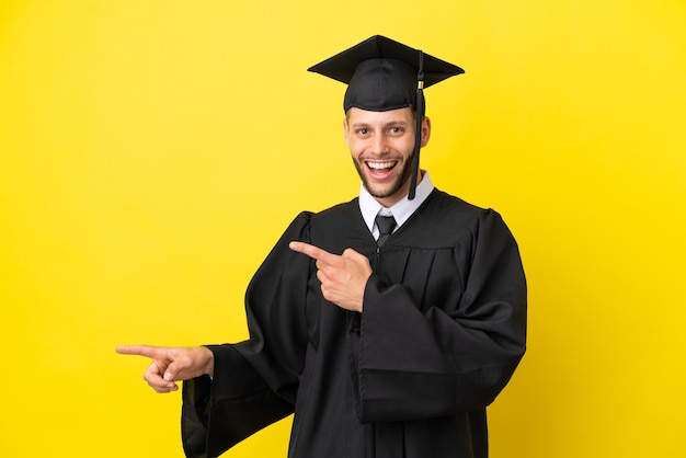 Young university graduate caucasian man isolated on yellow background surprised and pointing side