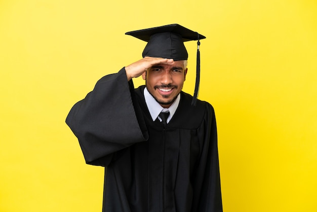 Young university graduate Colombian man isolated on yellow background looking far away with hand to look something